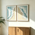 Shoreline diptych in pale wood frames above an oak cabinet in a sunlit room